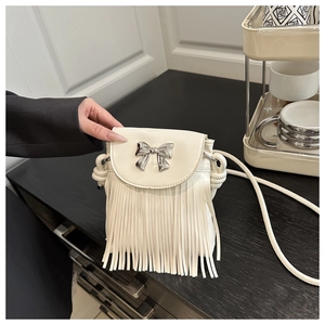Detail of off-white crossbody bag featuring a silver bow and long fringe tassels