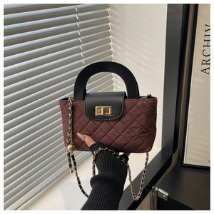 Detail of burgundy quilted bucket bag with black leather handle and gold twist lock