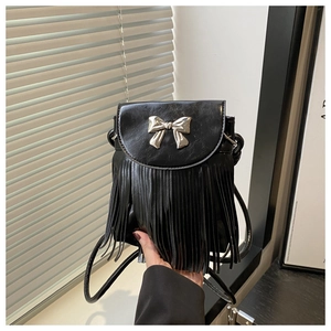 Detail of a black faux leather crossbody bag featuring a silver bow and long tassels