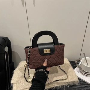 Brown quilted crossbody bag with black leather handle and golden chain on beige blanket