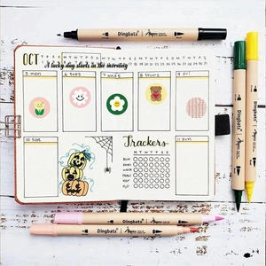 Flat lay of Dingbats planner with colorful twin-tip brush pens on white wood surface