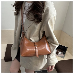 Close-up of brown glossy hobo bag with silver rivets and buckle on a beige blazer
