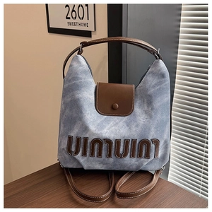 Detail of blue denim shoulder bag showing brown leather letter patches and top handle