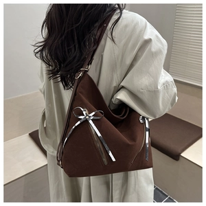 Detail of dark brown suede tote bag featuring silver bow accents and adjustable strap
