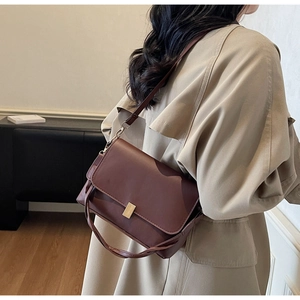 Detail of dark brown leather crossbody bag with gold buckle and pleated side accordion design