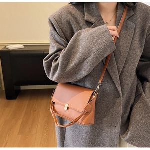 Détail d'un sac bandoulière en similicuir marron avec boucle dorée sur un blazer gris