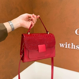 Red flap crossbody bag with crocodile texture and metal buckle on brown background