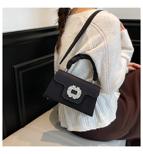 Detail of black satin handbag featuring a sparkling rhinestone floral buckle and ruched handle