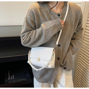 Detailed view of white crossbody bag with gold buckle and twisted handle on model