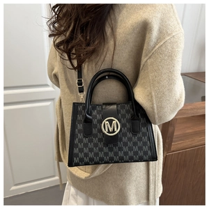 Detail van grijze M-patroon jacquard tas met gouden logo op beige wollen jas