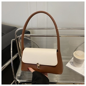 Detail of minimalist two-tone leather underarm bag with gold lock on a chic sofa