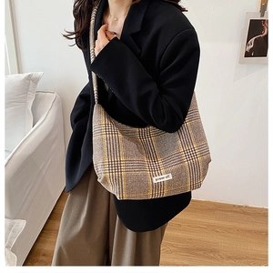 Model wearing a large capacity brown plaid crossbody bag with a power off patch detail