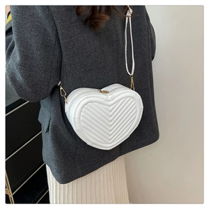 Detail of white heart-shaped crossbody bag with V-quilted texture on model