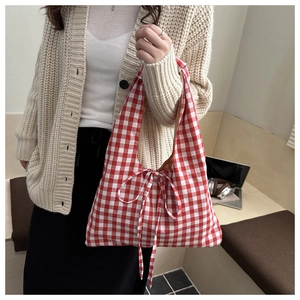 Detail of red gingham pattern fabric bag with decorative bow and woven texture