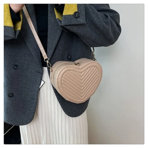 Model wearing a beige heart-shaped quilted crossbody bag over a dark blazer and white skirt