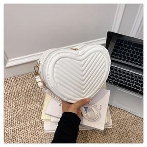 Detail of white heart-shaped crossbody bag with V-quilted texture and gold hardware