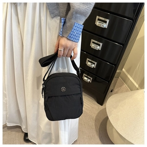 Detail of minimalist black nylon crossbody bag with silver M logo and adjustable strap