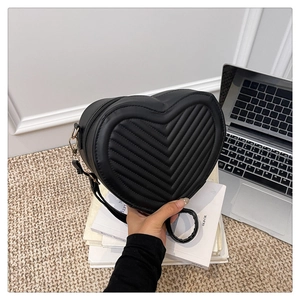 Detail showing the black heart-shaped crossbody bag with V-quilted texture and metal zipper