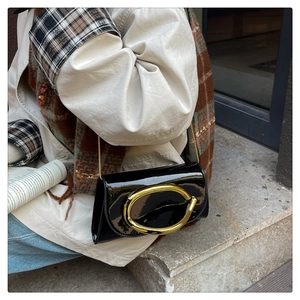Detail of glossy black patent leather shoulder bag with golden oval buckle and chain strap
