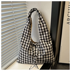 Detail of gingham shoulder bag featuring top knot handle and bow tie closure in sunlight