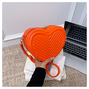 Macro detail of vibrant orange heart-shaped crossbody bag with V-quilted faux leather finish