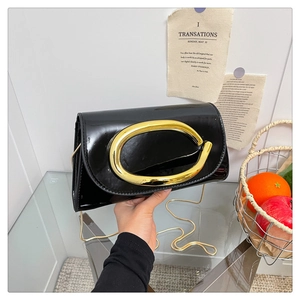 Detail of glossy black patent leather handbag with a large gold C-buckle and chain strap