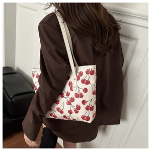 Détail d'un sac cabas beige avec imprimé cerise sur l'épaule et boucle dorée chic