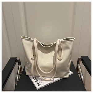 Detailed close-up of glossy cream-white tote bag on magazine with sleek patent finish