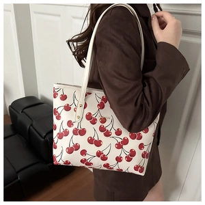Close-up of white tote bag with red cherry print and golden fashion text on shoulder