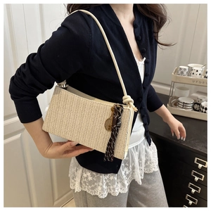 Detail of cream woven crossbody bag featuring textured straw finish and tassel accent