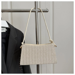 Detail of beige herringbone woven underarm bag with slim leather straps and metal tips