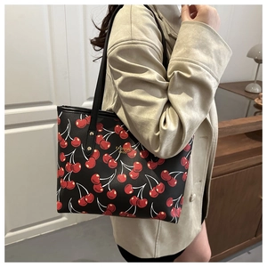 Détail du sac cabas en PU noir avec imprimé cerise et logo doré porté par le mannequin