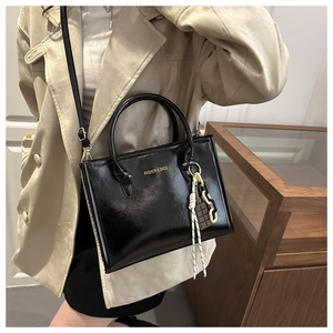 Detail of black glossy PU leather tote bag with gold lettering and decorative chain charm