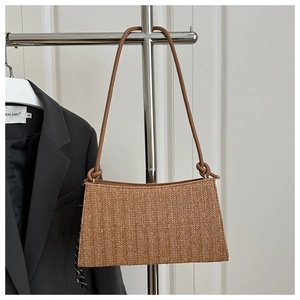 Detail of woven brown underarm bag with knotted leather strap on a minimal background