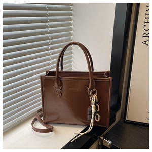 Detail of coffee brown leather tote bag with gold lettering and decorative chain
