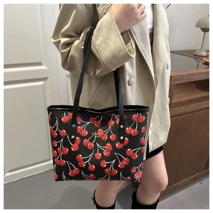 Detail of black cherry print tote bag with gold studs shown on a model's shoulder