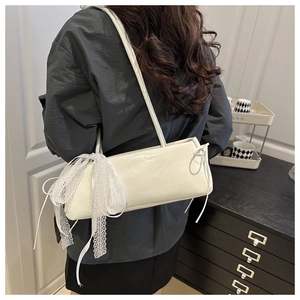 Detail of white leather shoulder bag with oversized lace bow and sleek shoulder strap