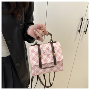 Close-up of pink checkered backpack featuring cartoon dog art and dark brown leather straps