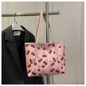 Close-up of pink cherry print tote bag with gold lettering hanging on a metal rack