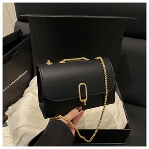 Détail du sac bandoulière noir avec fermoir ovale doré sur un coffret cadeau