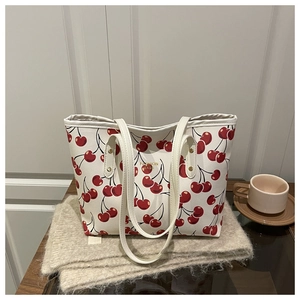 Détail du sac cabas crème avec imprimé cerises, texte doré et rivets métalliques