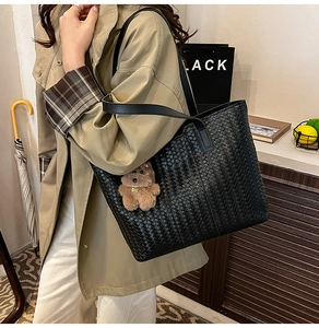Detail of black woven leather tote bag with brown plush bear charm worn by a model