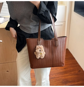 Detail of a brown woven leather tote bag with slim straps and a plush bear pendant