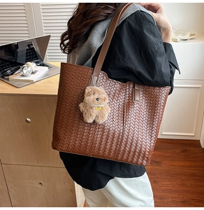 Detail of dark brown woven tote bag featuring leather stripes and cute plush bear charm