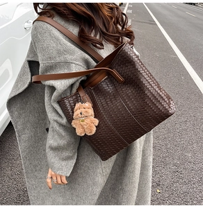 Detail of dark brown woven tote bag with a plush bear charm on a grey wool coat