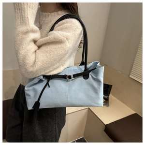 Close-up of light blue canvas tote bag with black leather straps on white sweater