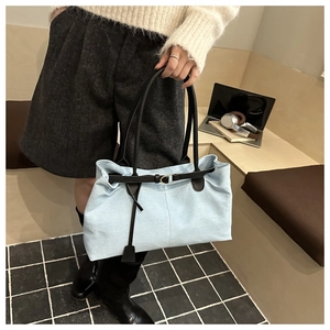 Detail of light blue canvas tote bag featuring black contrast straps and metal buckle accent