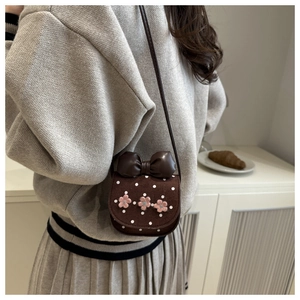 Détail d'un mini sac bandoulière avec fleurs au crochet roses et un grand nœud en cuir brun