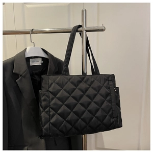 Close-up of black quilted tote bag with side pockets displayed next to a black blazer