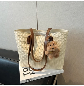 Detailed view of a cream woven tote bag with brown straps and a plush dog charm on a sofa